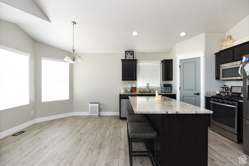 Kitchen with stainless steel appliances, a chandelier, light stone counters, light wood finished floors, and recessed lighting