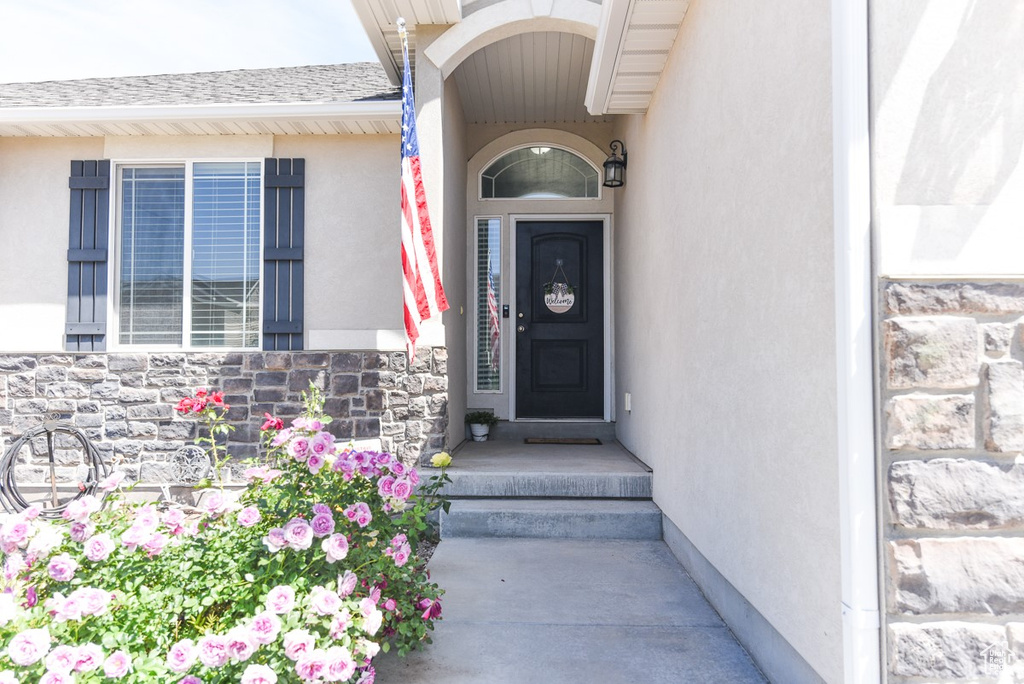 View of exterior entry featuring stone siding, stucco siding, and roof with shingles