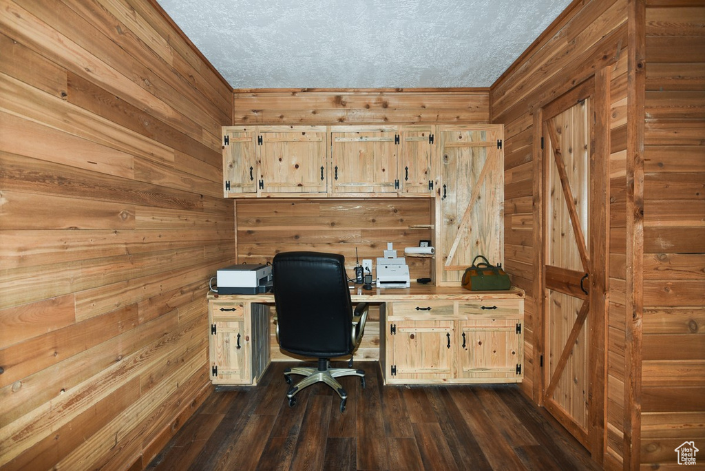Office area with wooden walls, a textured ceiling, and dark wood-style floors