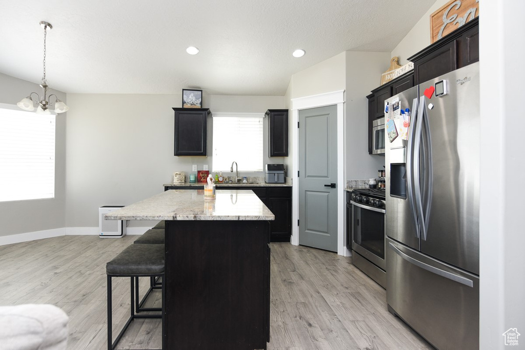 Kitchen featuring stainless steel appliances, a kitchen island, a breakfast bar, light wood finished floors, and a chandelier