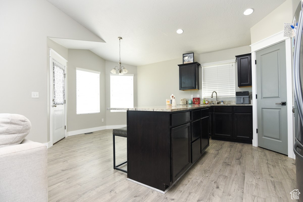 Kitchen with a breakfast bar, a chandelier, light wood finished floors, dark cabinetry, and recessed lighting