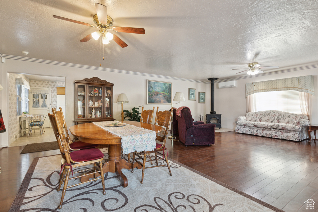 Dining area with a wood stove, ceiling fan, a textured ceiling, wood finished floors, and an AC wall unit