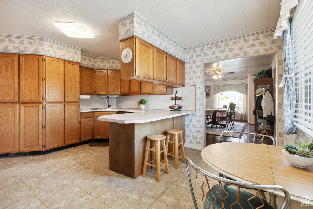 Kitchen featuring wallpapered walls, a peninsula, light countertops, brown cabinets, and ceiling fan