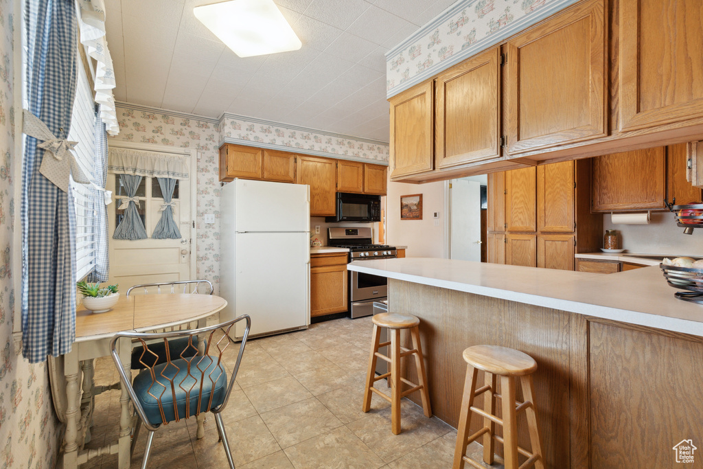 Kitchen with freestanding refrigerator, black microwave, gas range, wallpapered walls, and light countertops
