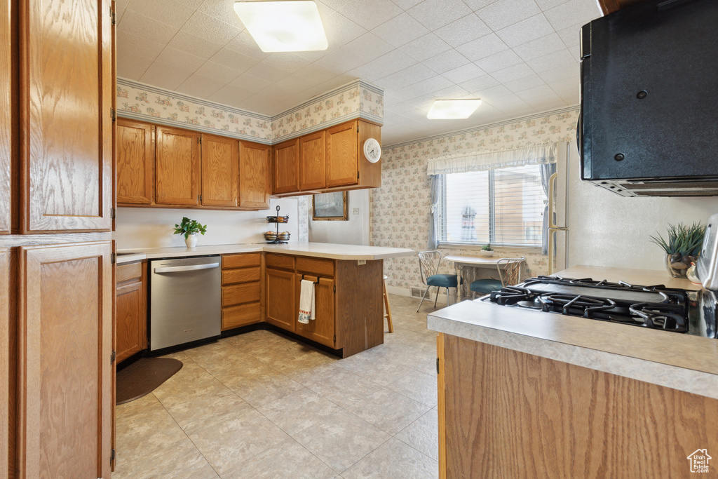 Kitchen featuring dishwasher, wallpapered walls, a peninsula, light countertops, and brown cabinetry