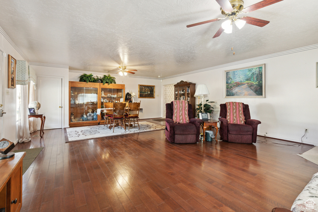 Living room featuring ceiling fan, wood finished floors, crown molding, a textured ceiling, and baseboards