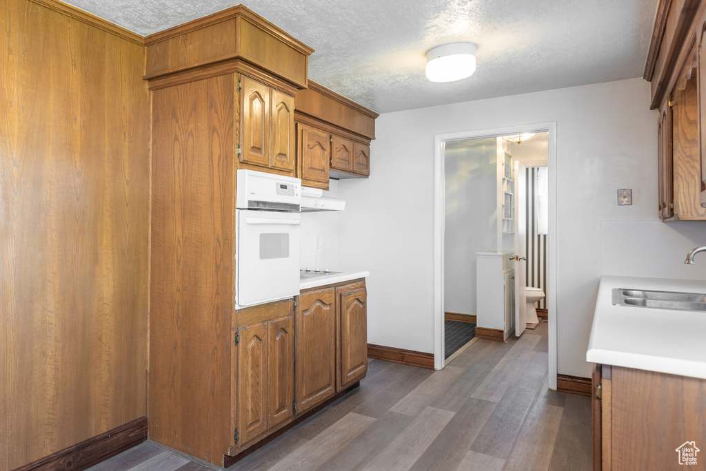 Kitchen featuring a sink, oven, light countertops, a textured ceiling, and brown cabinetry