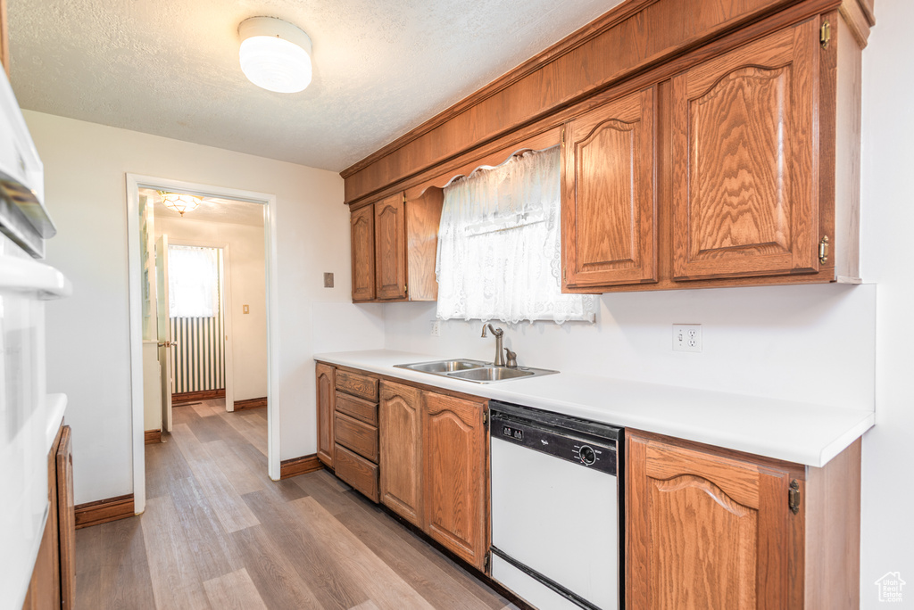 Kitchen featuring white dishwasher, a sink, light wood-style flooring, light countertops, and brown cabinetry