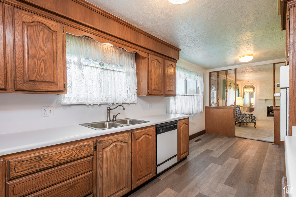 Kitchen featuring white dishwasher, a sink, a textured ceiling, brown cabinets, and wood finished floors