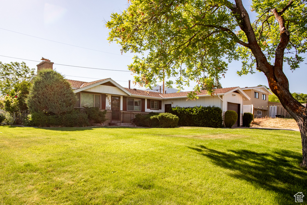 Single story home with an attached garage, a chimney, a front yard, and board and batten siding