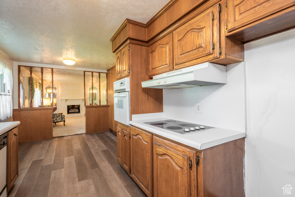 Kitchen with white oven, under cabinet range hood, a textured ceiling, light countertops, and dark wood-style flooring
