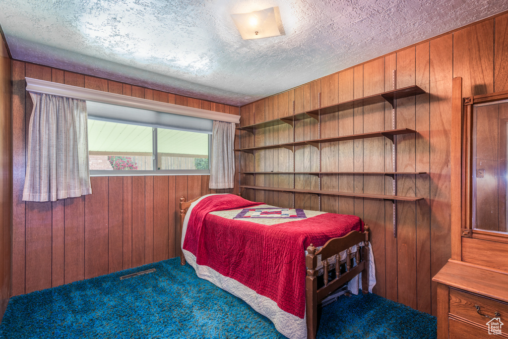 Carpeted bedroom featuring wooden walls and a textured ceiling