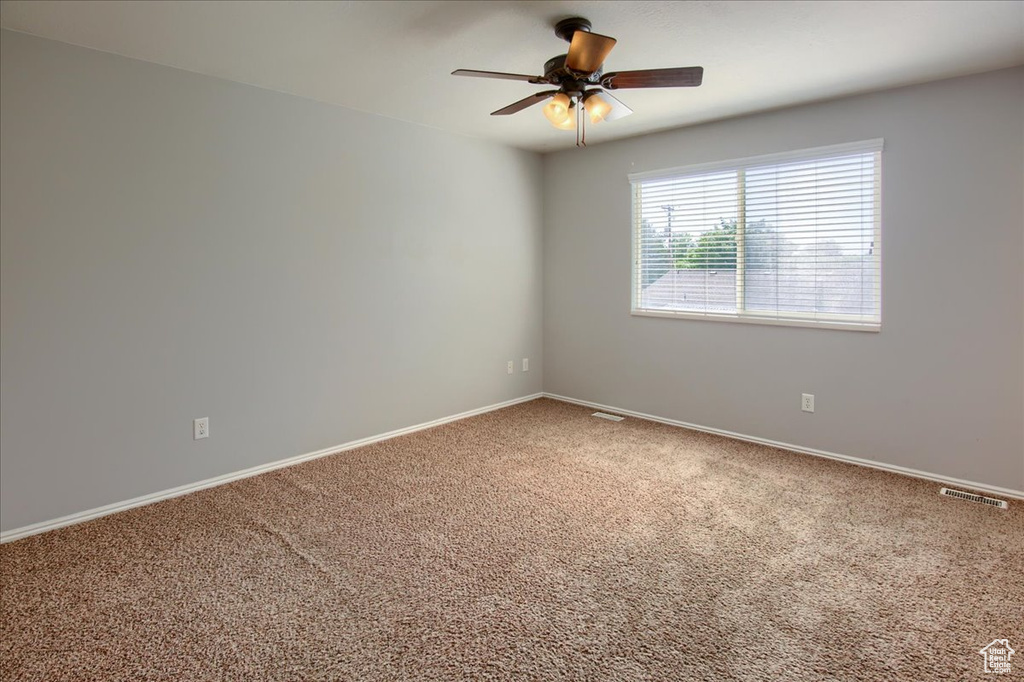 Carpeted spare room featuring ceiling fan and baseboards
