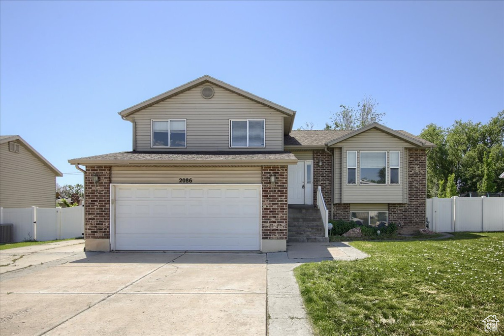 View of front facade with driveway, an attached garage, brick siding, cooling unit, and roof with shingles