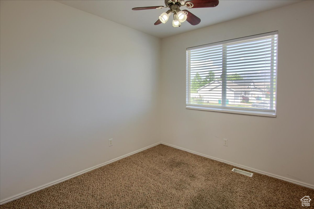Carpeted spare room with a ceiling fan and baseboards