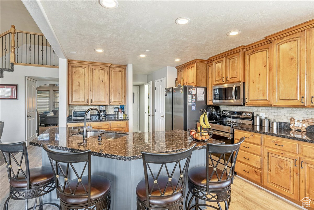 Kitchen with stainless steel appliances, a sink, light wood-style floors, a kitchen breakfast bar, and dark stone countertops