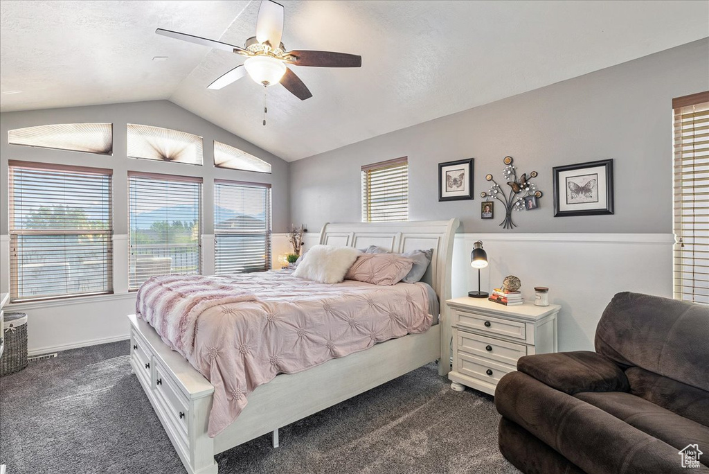 Bedroom featuring dark carpet, multiple windows, lofted ceiling, and a ceiling fan