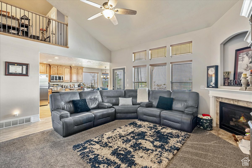 Living room featuring ceiling fan, high vaulted ceiling, a tile fireplace, and light carpet