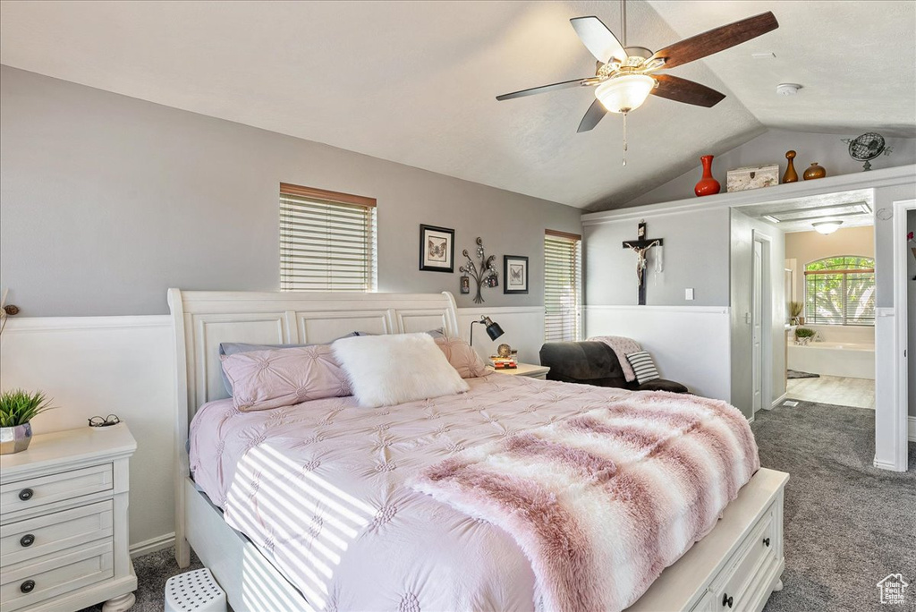 Bedroom with dark colored carpet, lofted ceiling, multiple windows, connected bathroom, and a ceiling fan
