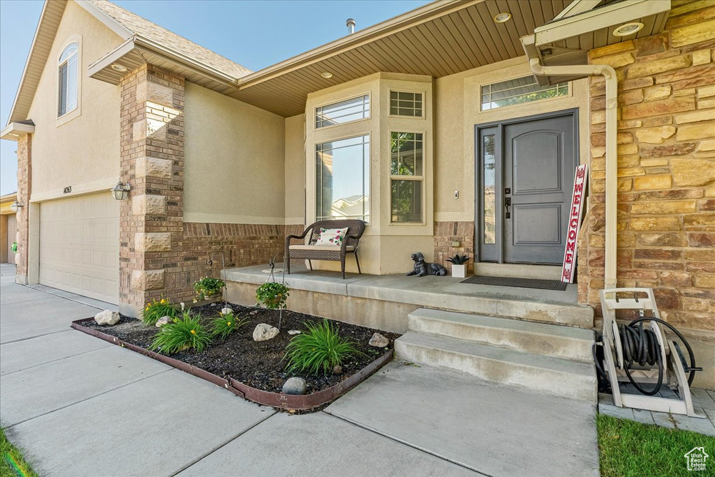 Doorway to property featuring stucco siding, a garage, concrete driveway, covered porch, and brick siding