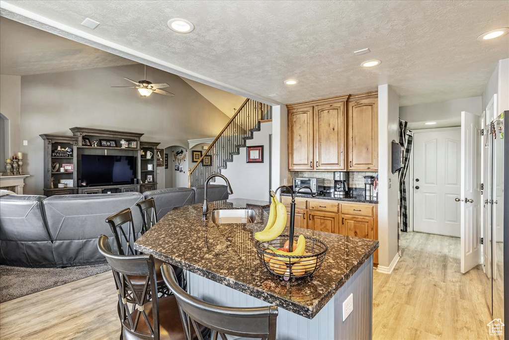 Kitchen with a sink, light wood-type flooring, a kitchen bar, ceiling fan, and dark stone countertops