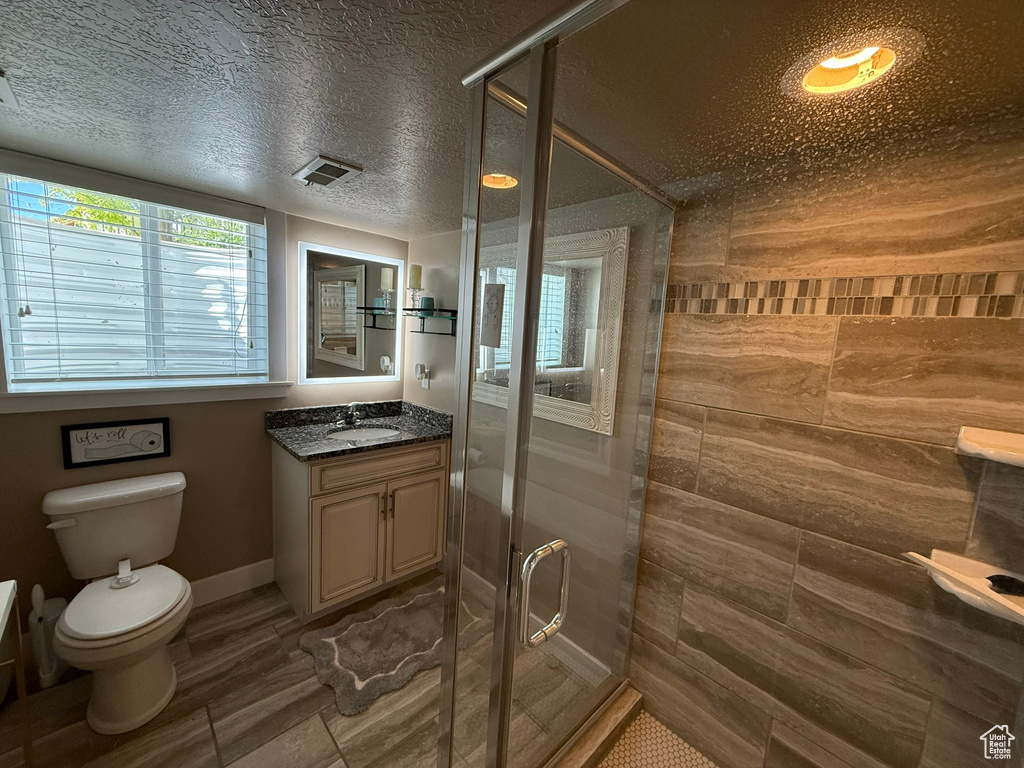 Bathroom featuring vanity, toilet, a shower stall, a textured ceiling, and baseboards