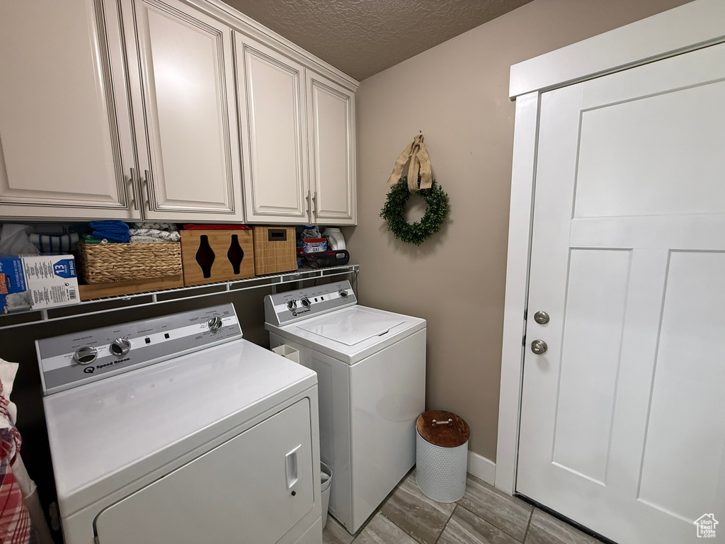 Washroom featuring cabinet space, washing machine and clothes dryer, a textured ceiling, light wood-style floors, and baseboards