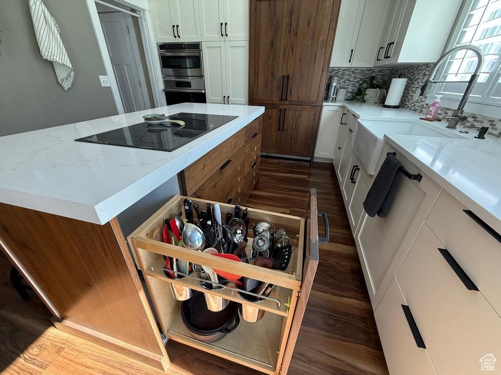 Kitchen featuring black electric cooktop, double oven, dark wood-style flooring, and decorative backsplash