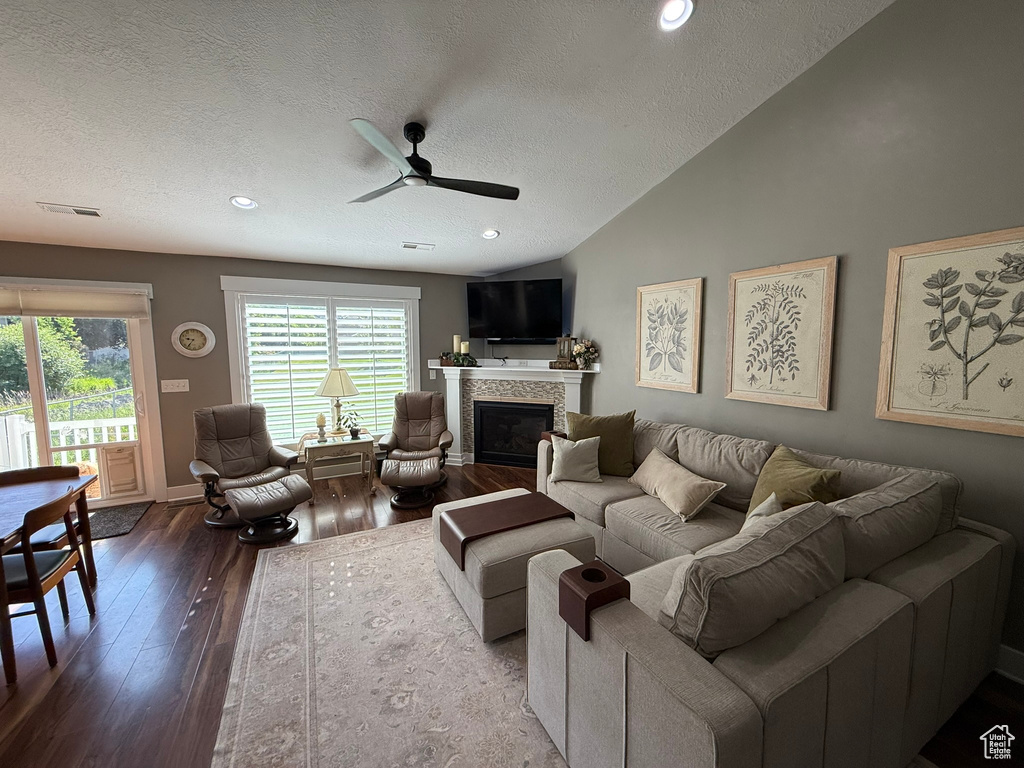 Living area with ceiling fan, a fireplace, a textured ceiling, hardwood / wood-style flooring, and lofted ceiling