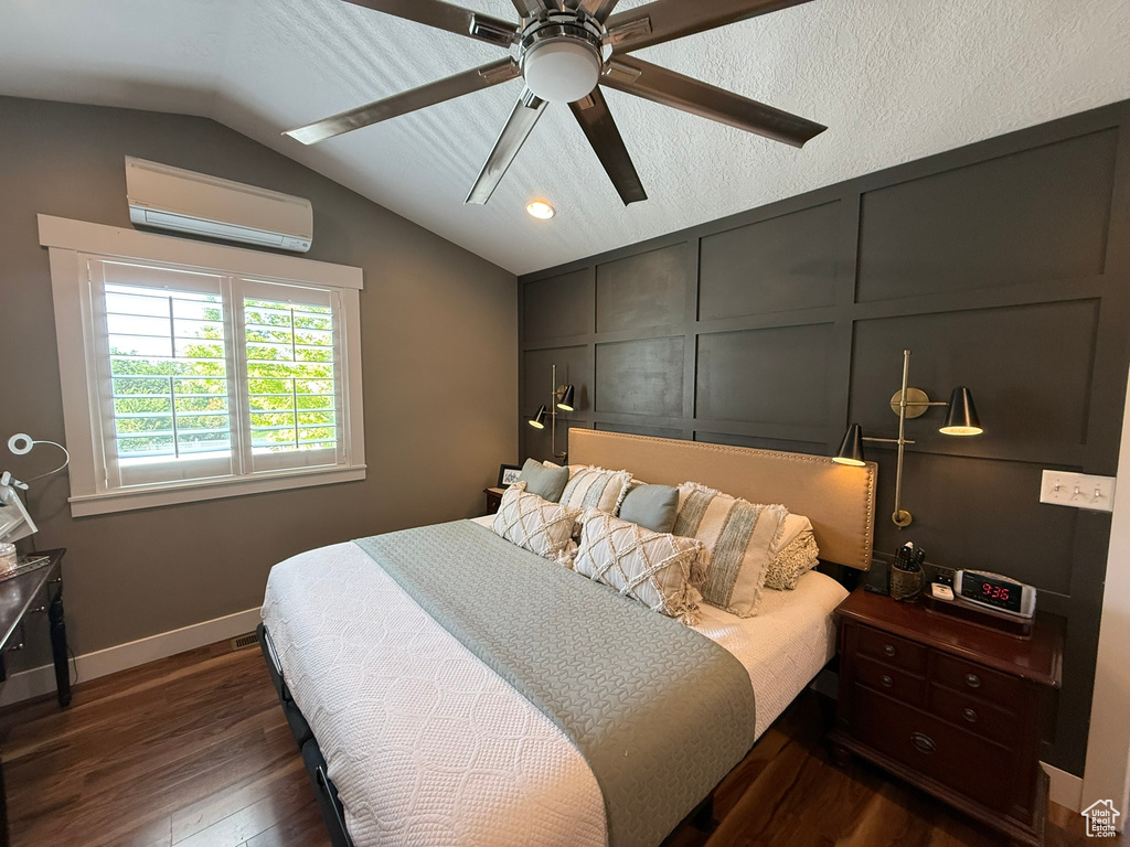Bedroom with a wall unit AC, dark wood-type flooring, lofted ceiling, a decorative wall, and baseboards