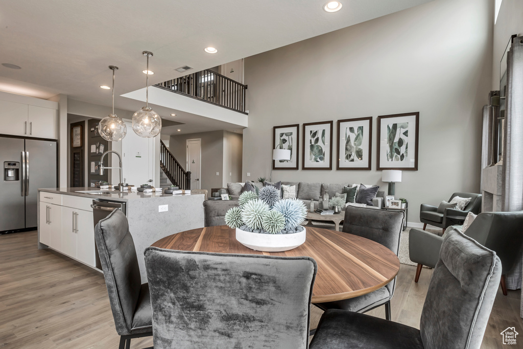 Dining area with light wood-style floors, stairs, recessed lighting, and a high ceiling
