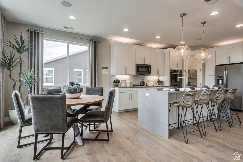 Kitchen featuring appliances with stainless steel finishes, light wood-type flooring, a kitchen bar, tasteful backsplash, and white cabinets