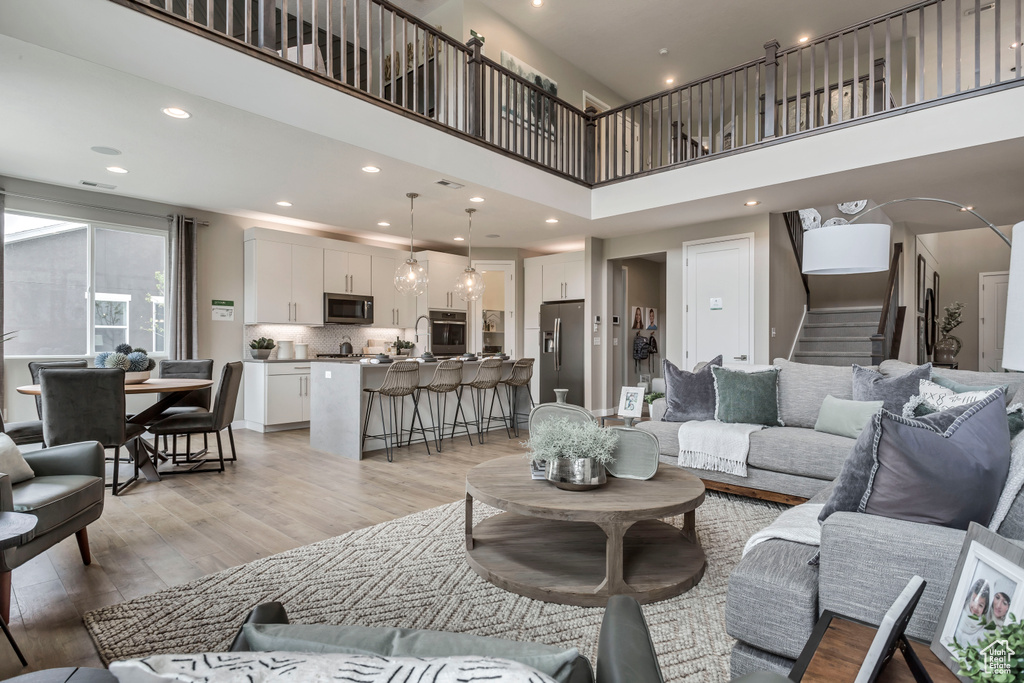 Living area with light wood finished floors, a towering ceiling, stairs, and recessed lighting