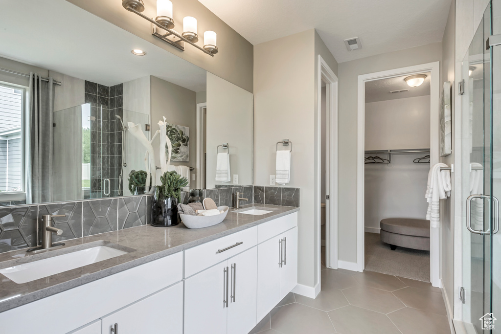 Bathroom with a shower stall, double vanity, a walk in closet, baseboards, and tile patterned flooring