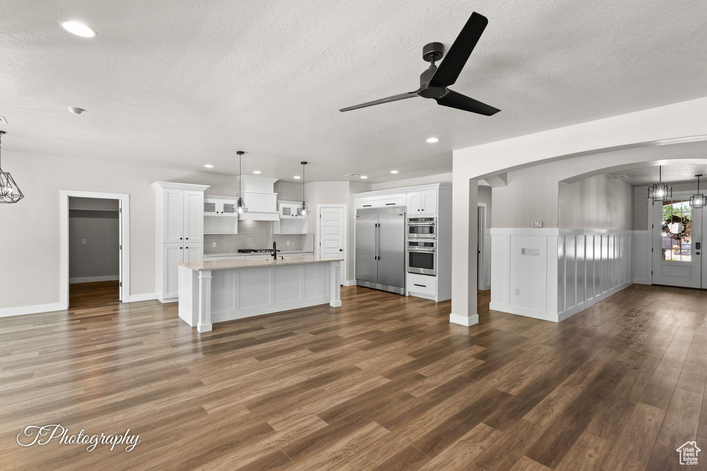Unfurnished living room with a ceiling fan, a textured ceiling, arched walkways, dark wood finished floors, and a chandelier