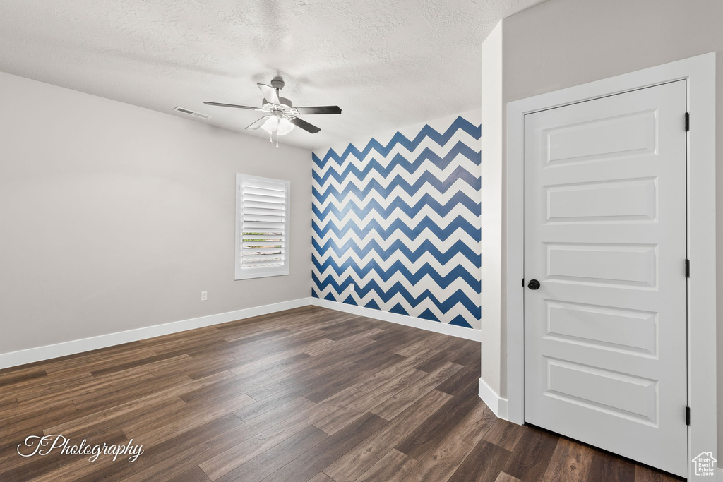 Empty room with a ceiling fan, baseboards, an accent wall, dark wood-style floors, and a textured ceiling