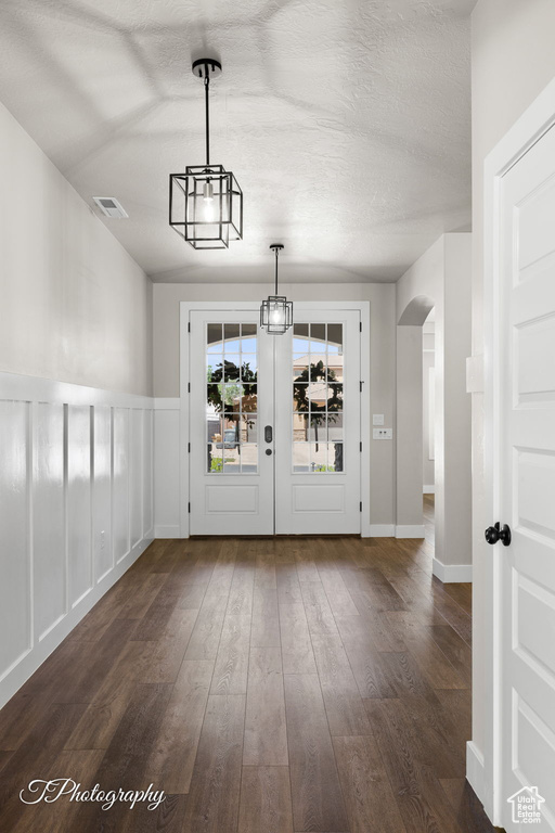 Unfurnished dining area with arched walkways, dark wood-style floors, and a textured ceiling