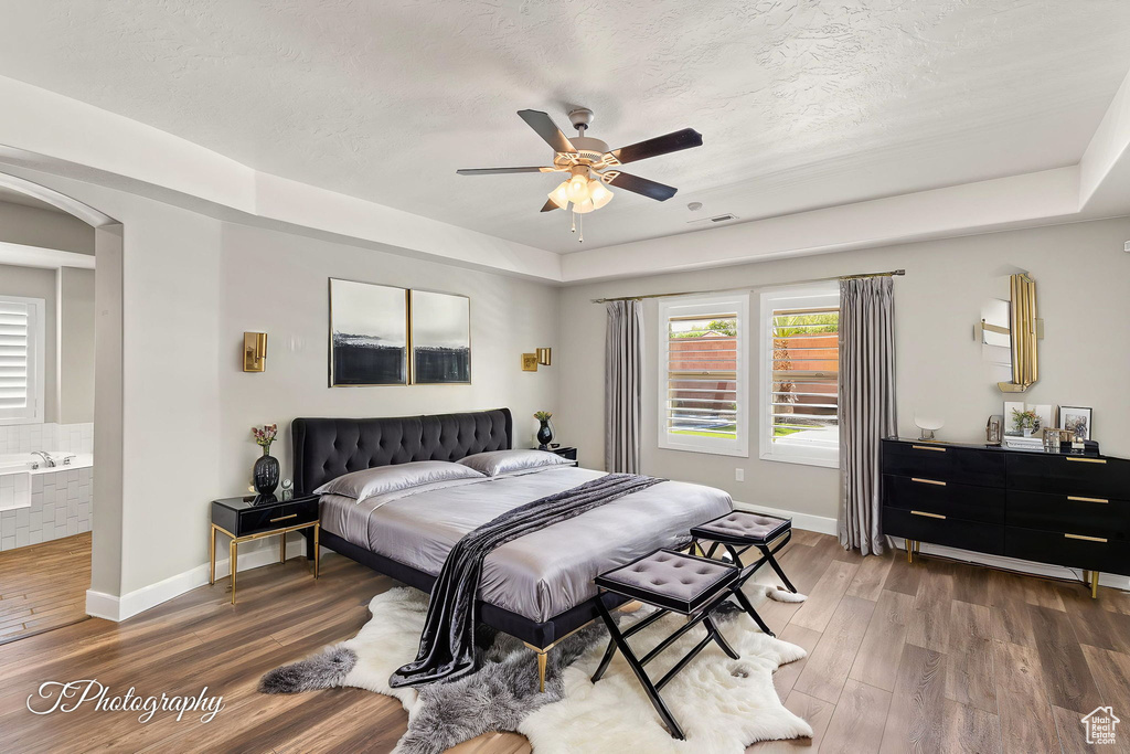 Bedroom featuring arched walkways, wood finished floors, baseboards, a textured ceiling, and a ceiling fan