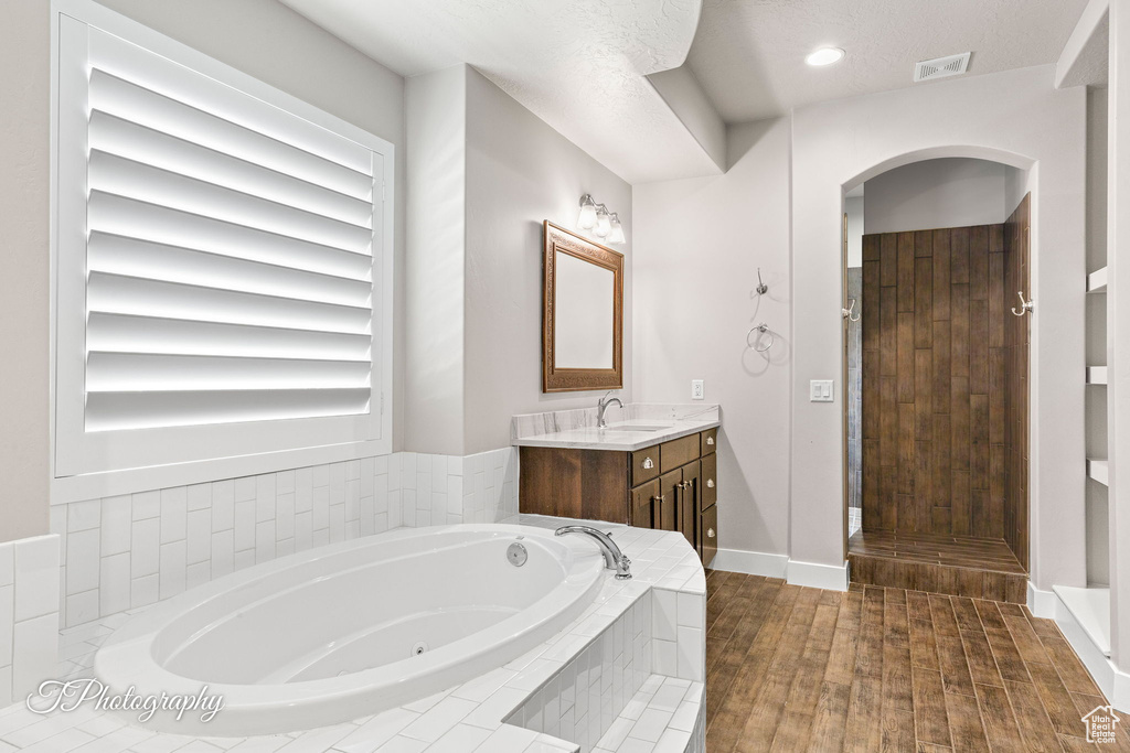 Bathroom with vanity, a jetted tub, wood finished floors, baseboards, and recessed lighting
