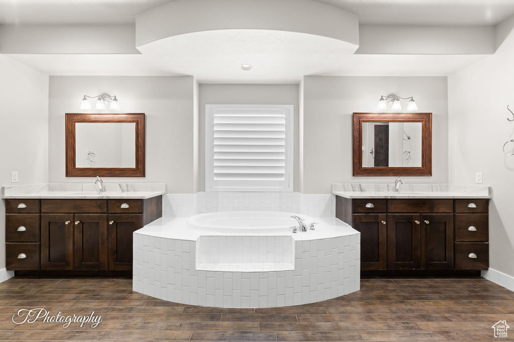 Full bath featuring two vanities, a garden tub, and wood finished floors