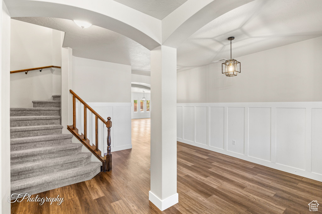 Stairway featuring arched walkways, a decorative wall, wood finished floors, and a wainscoted wall