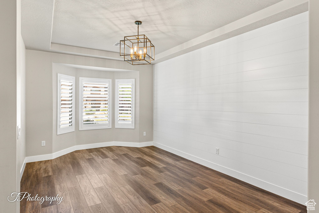 Spare room featuring a chandelier, dark wood-style floors, baseboards, and a textured ceiling