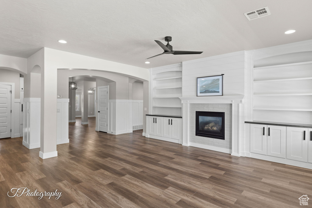 Unfurnished living room featuring a ceiling fan, wood finished floors, a glass covered fireplace, recessed lighting, and built in features