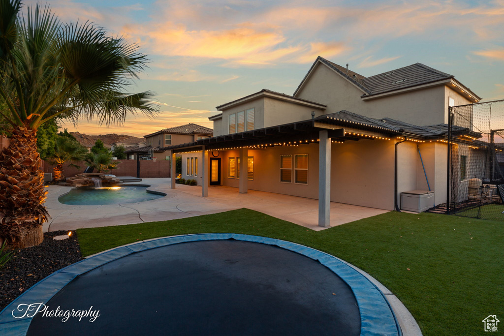 Back of property at dusk with stucco siding, a patio area, and a hot tub