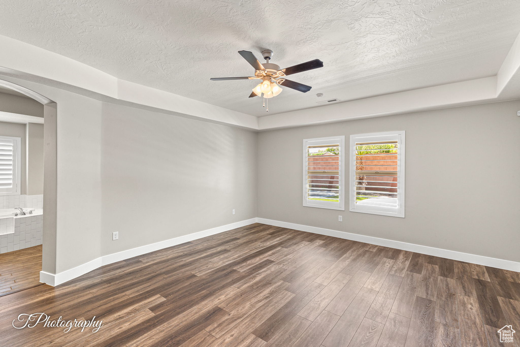 Empty room featuring dark wood-style flooring, a ceiling fan, arched walkways, a textured ceiling, and baseboards