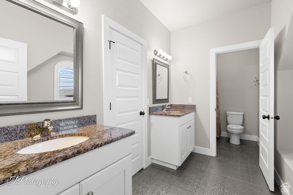 Bathroom featuring two vanities, toilet, and baseboards
