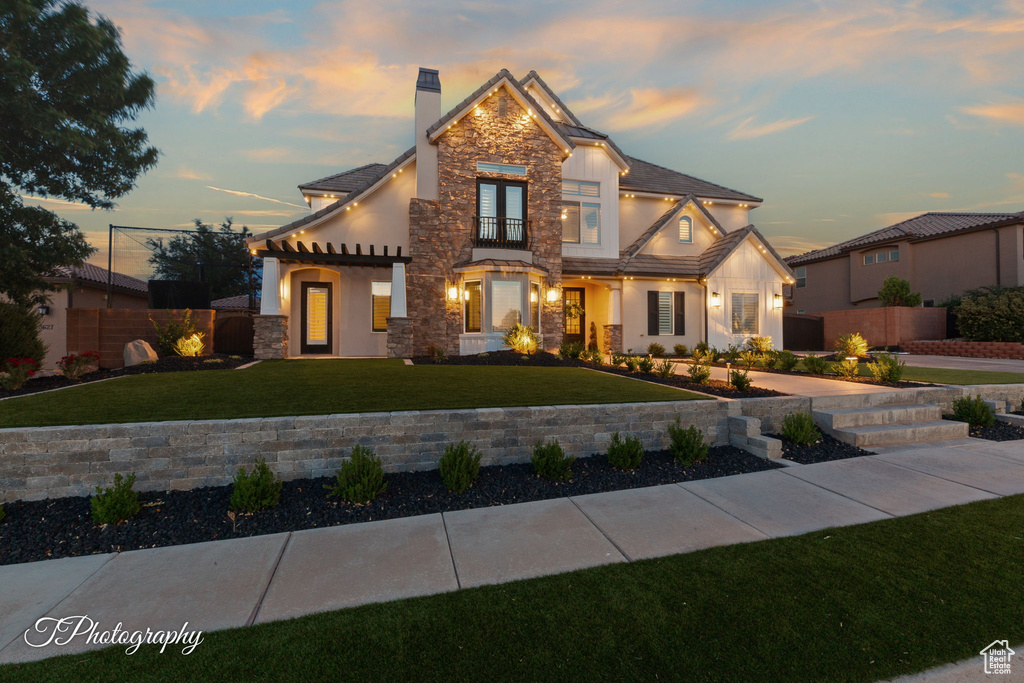 View of front facade featuring a chimney, stone siding, stucco siding, and a balcony