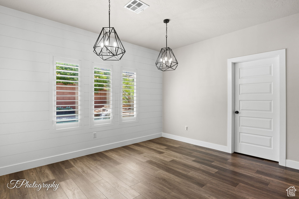 Unfurnished room with a chandelier, baseboards, and dark wood-style flooring