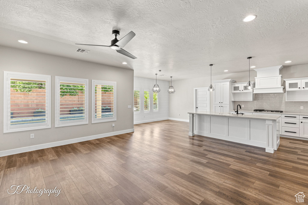 Unfurnished living room with a sink, ceiling fan, baseboards, dark wood-type flooring, and a textured ceiling