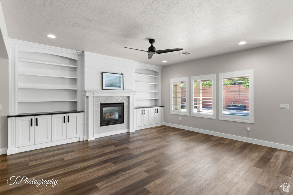 Unfurnished living room featuring a textured ceiling, a ceiling fan, dark wood-style floors, baseboards, and a fireplace